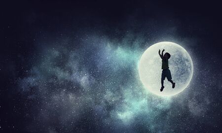 Silhouette of happy boy jumping to touch full moon. Mixed mediaの写真素材