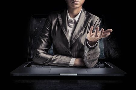 Businesswoman with opened palm coming out from the screen of laptop. Mixed mediaの写真素材