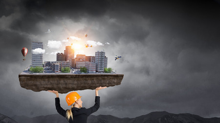 Builder woman lifting city exterior model above head. Mixed mediaの写真素材