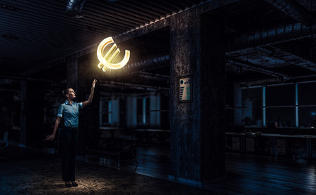 Businesswoman in dark office touching glowing euro sign. Mixed mediaの写真素材