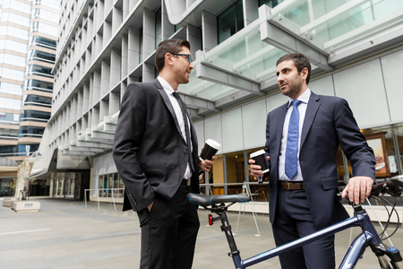 Two young businessmen with a bike in city centreの写真素材