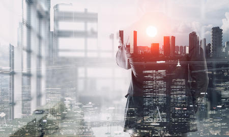 Young businessman with his back looking at city and talking mobile phone. Mixed mediaの写真素材