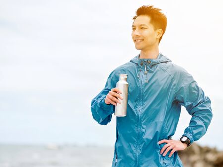 Young man in sport clothes drinking water after workout on the beachの写真素材