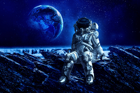 Astronaut sitting on cliff edge against dark starry sky.の写真素材