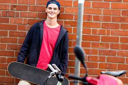 Teenage boy with skateboard standing next to the wall