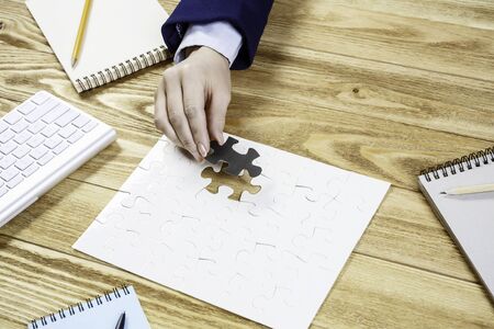 Hand of businesswoman completing puzzle with missing piece