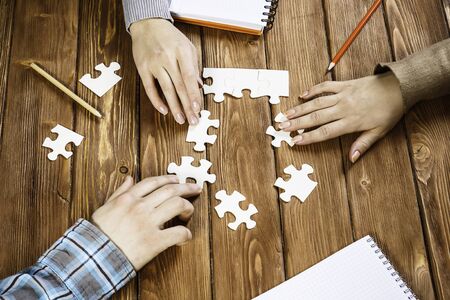 Group of people sitting at table and assembling jigsaw puzzleの写真素材