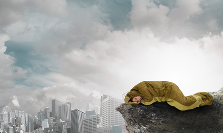 Young woman lying in sleeping bag on rock edge. Mixed mediaの写真素材