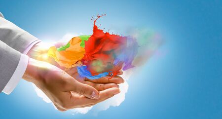 Close up of hand holding splashes of colorful paintの写真素材