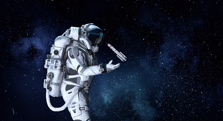 Astronaut on starry background holding rocket in palm. Mixed media