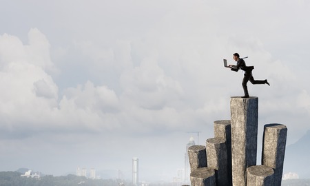 Businessman with laptop in hands running on stone graph. Mixed mediaの写真素材