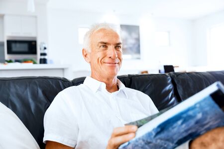Handsome sennior man reading a book relaxing on a sofaの写真素材