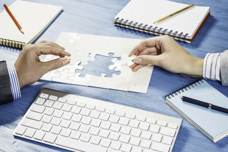 Business people sitting at table and assembling jigsaw puzzle