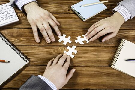 Group of business people sitting at table and assembling jigsaw puzzle