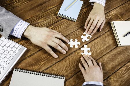 Group of business people sitting at table and assembling jigsaw puzzle