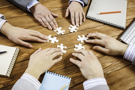 Group of business people sitting at table and assembling jigsaw puzzleの写真素材