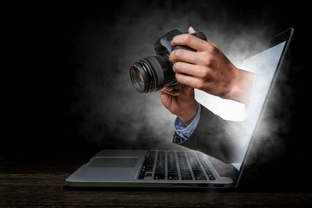 Hands of businessman with photo camera coming from laptop screen. Mixed media