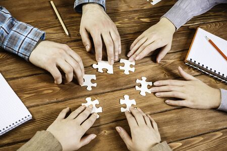 Group of people sitting at table and assembling jigsaw puzzleの写真素材