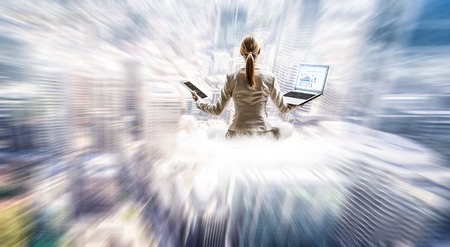 Businesswoman sitting in lotus pose on cloud high in skyの写真素材