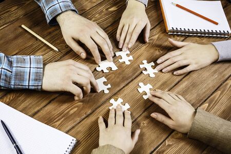 Group of people sitting at table and assembling jigsaw puzzle