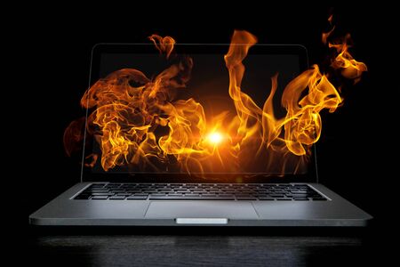 Open laptop with fire flames coming from screen on dark background. Mixed mediaの写真素材