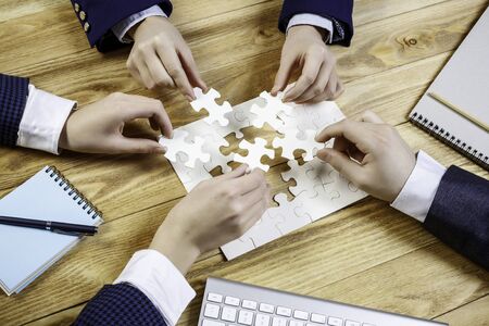 Group of business people sitting at table and assembling jigsaw puzzleの写真素材