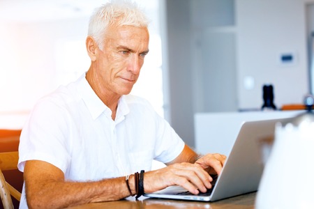 Senior handsome man in casual clothes working on laptop at homeの写真素材