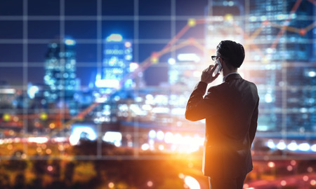 Elegant businessman against modern cityscape talking his mobile phoneの写真素材