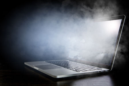 Open laptop with fume coming from screen on dark background. Mixed mediaの写真素材