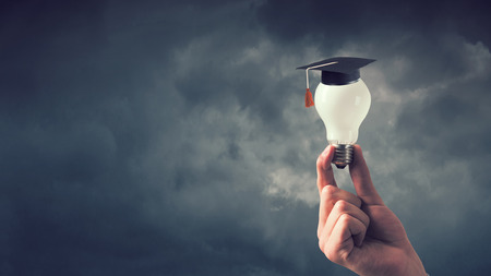 Hand of businessman holding glowing light bulb with graduation hat on itの写真素材