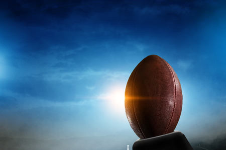 Night football arena in lights and flashes with american football ball on the foregroundの写真素材