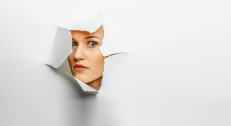 Woman looking out from a hole of torn paperの写真素材