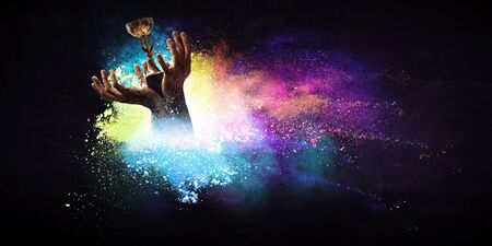 Hands holding champion cup on colourful splashes background. Mixed mediaの写真素材