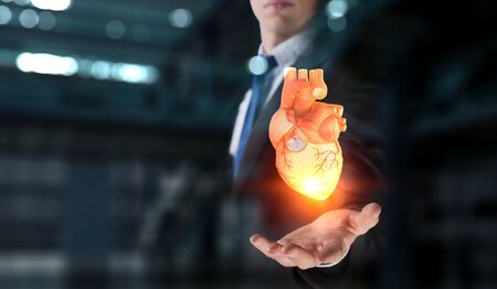 Man`s hands showing anatomical heart model. Mixed media.の写真素材