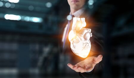 Man`s hands showing anatomical heart model. Mixed media.の写真素材