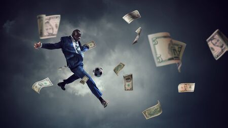 Black businessman plays football with dollar banknotes aroundの写真素材