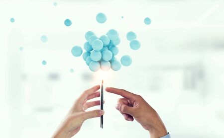 Businessman hands holding a smartphone with a bunch of colourful spheres levitating above. Mixed...