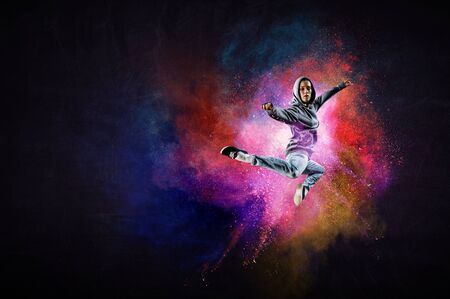 Modern female dancer jumping in hoodie with colourful splashes background. Mixed media
