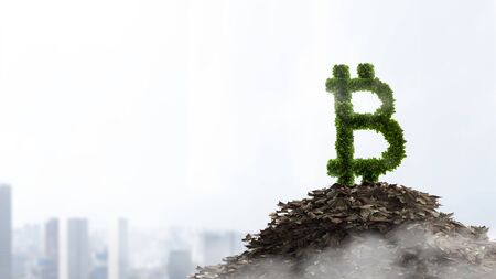 Bitcoin symbol made of green leaves on a tree, with a pile of dead leaves below, daytime cityscape backgroundの写真素材