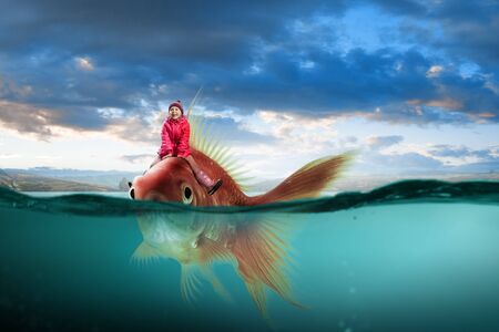 Cute kid girl riding gold fish in clear blue waterの写真素材