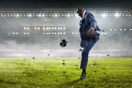 Black businessman playing footbal on a night stadium with burning lightsの写真素材