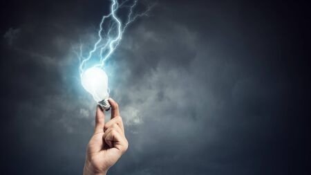 Business hand holding glowing light bulb with lightning