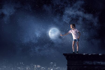 Cute girl of school age touching moon planet. Mixed mediaの写真素材