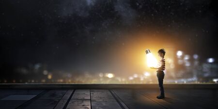 Boy of school age with big glowing bulb in hands. Mixed mediaの写真素材
