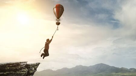 Cheerful kid on hot air balloon in the sky. Mixed mediaの写真素材