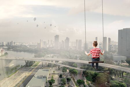 Cute kid boy riding swing high in blue sky. Mixed mediaの写真素材