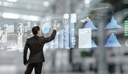 Back of businessman in office drawing media graphs on screen. Mixed media