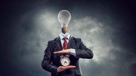 Businessman with light bulb instead of head and clock in hands. Mixed mediaの写真素材