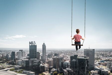 Cute kid boy riding swing high in blue sky. Mixed mediaの写真素材