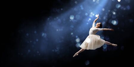 Elegant woman dancer in white dress against dark backgroundの写真素材